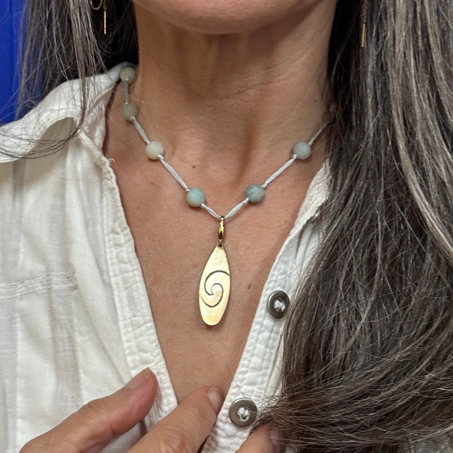 Necklace with a gold pendant worn by a person in a white shirt.