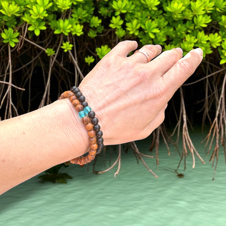 2 blue mind bracelets on hand near mangroves and water