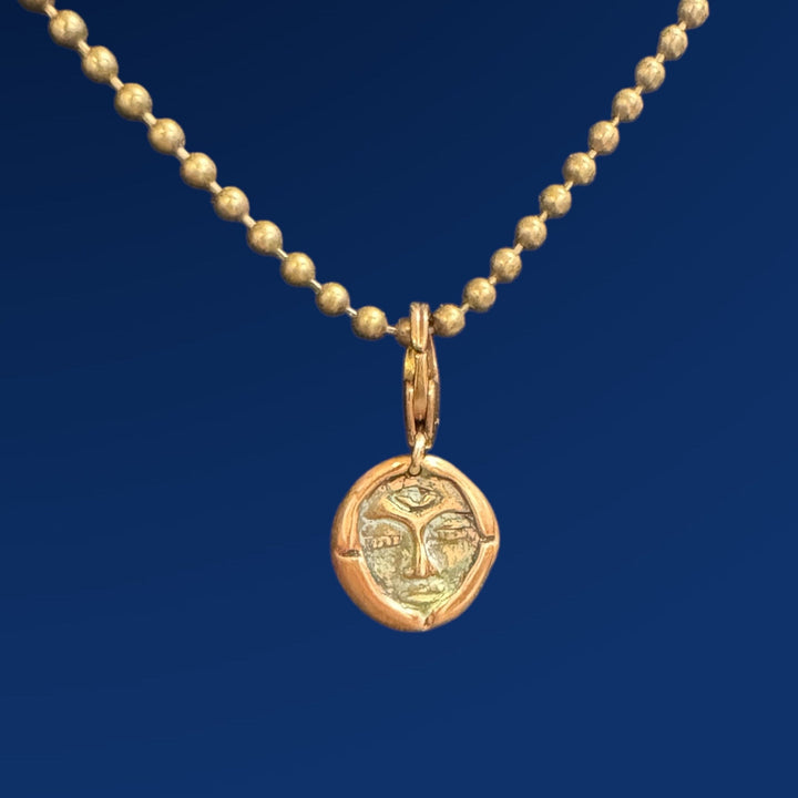 bronze emerge charm on chain on blue background