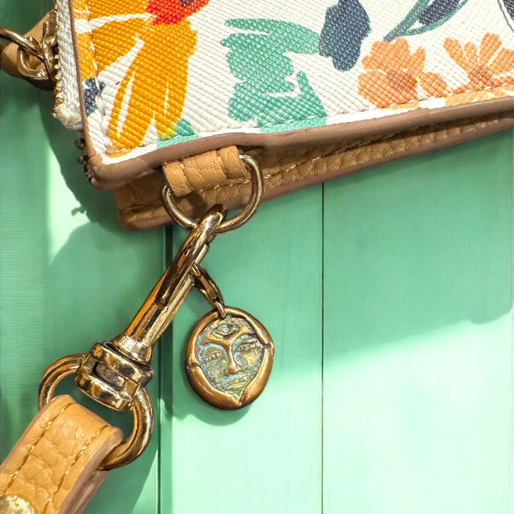 bronze emerge charm clipped to a floral purse on a turquoise table