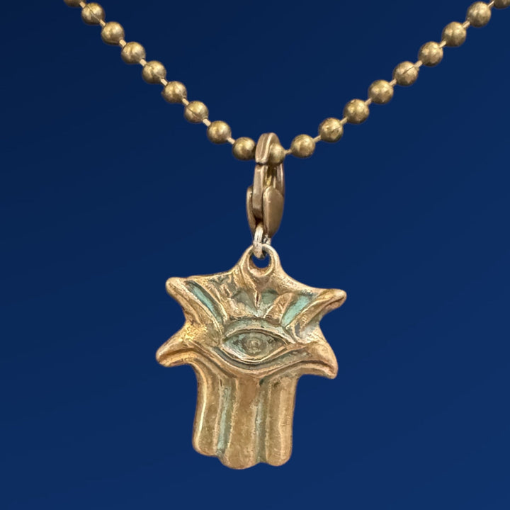 bronze hamsa with evil eye on gold chain and blue background