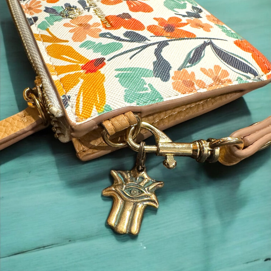 Floral-patterned pouch with a keychain and hamsa hand charm on a teal surface