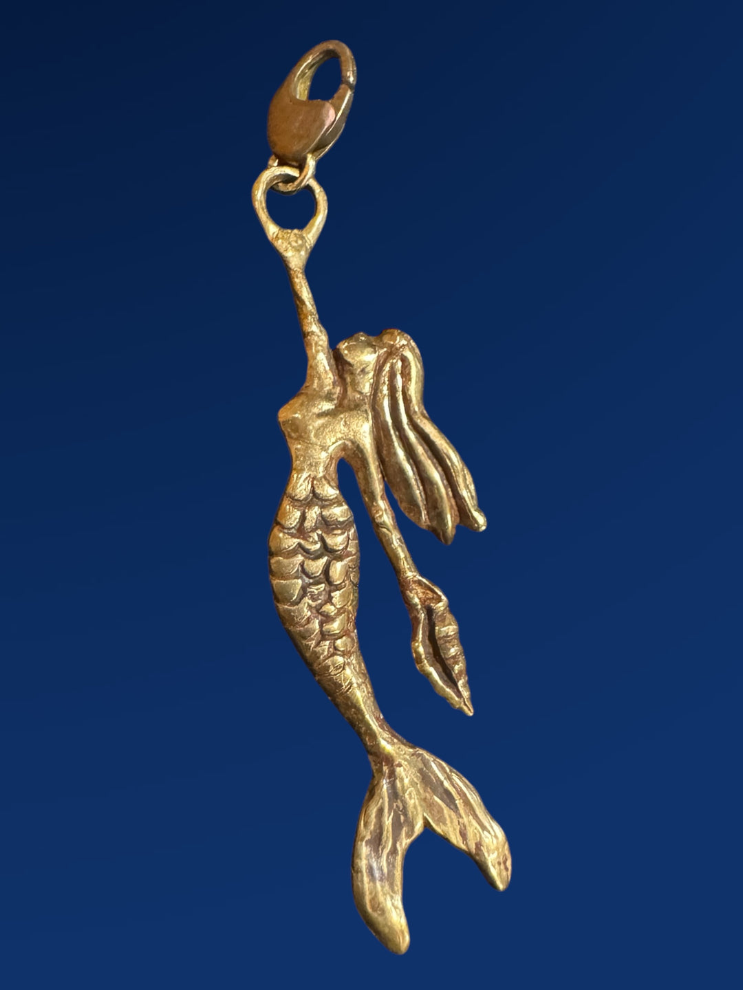 Gold mermaid charm on a blue background