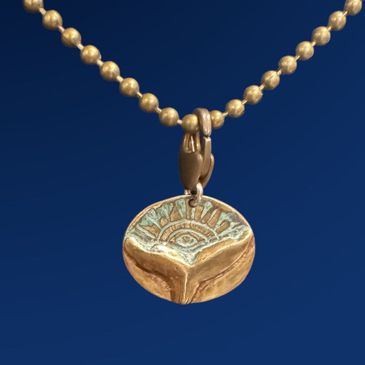 gold whale tail with eye charm on chain on blue background
