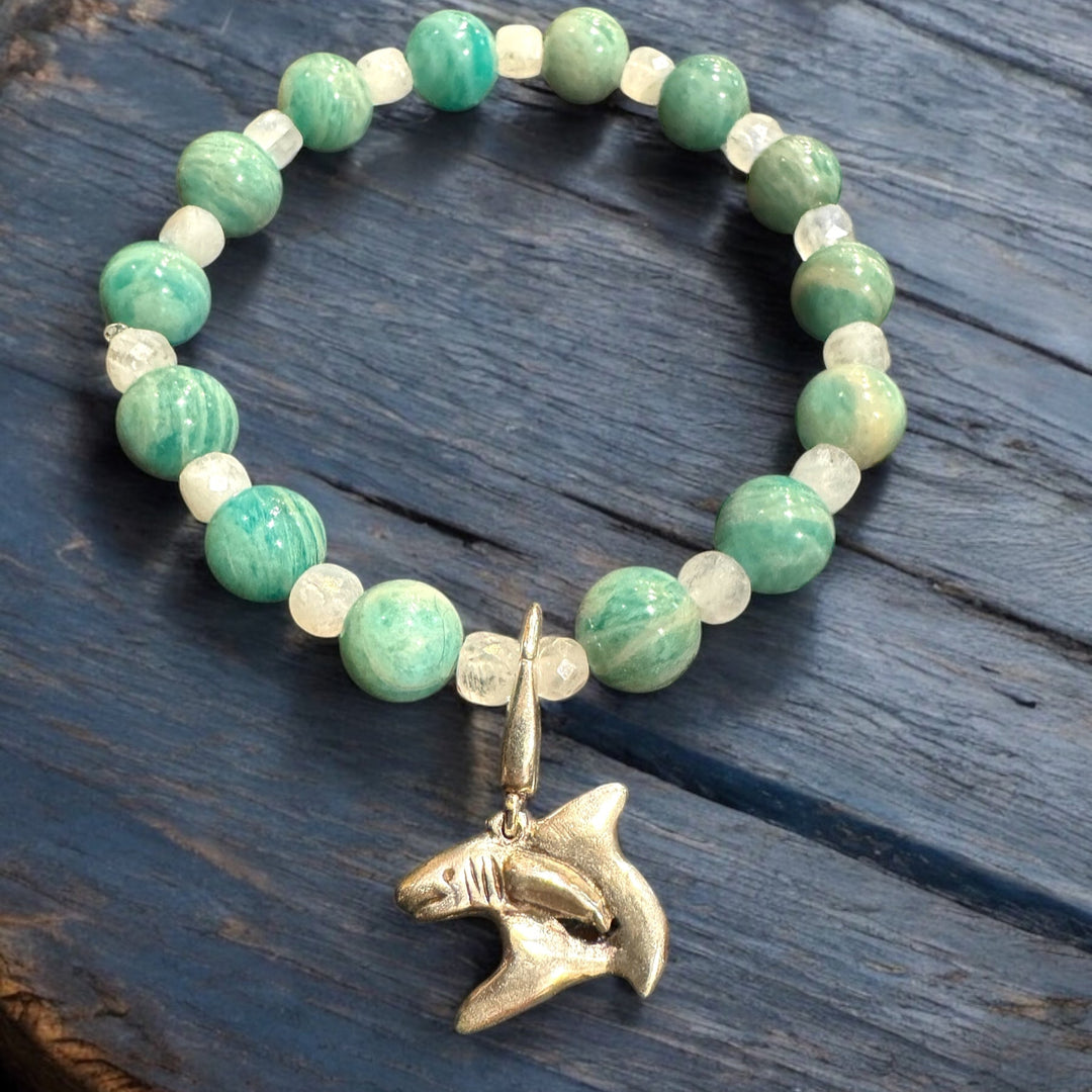 Bracelet with green beads and a shark pendant on a wooden surface