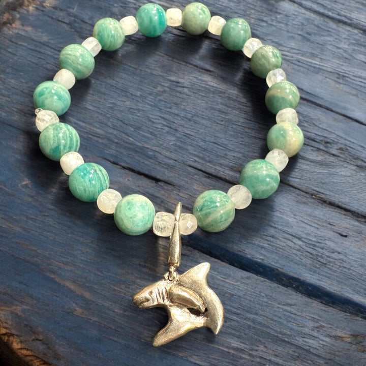 Bracelet with green beads and a shark pendant on a wooden surface