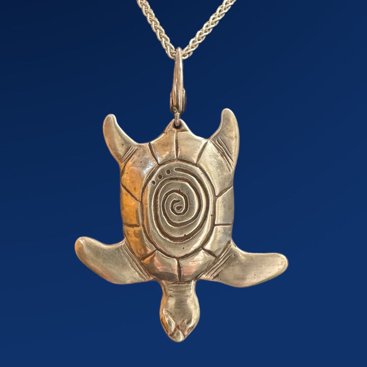 Turtle-shaped pendant with spiral design on a chain against a blue background