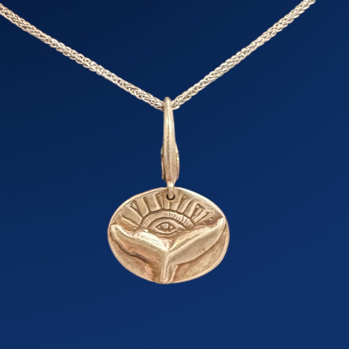 silver whale tail with eye charm on chain on blue background
