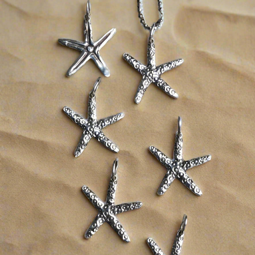 Silver sea star charms on sand background