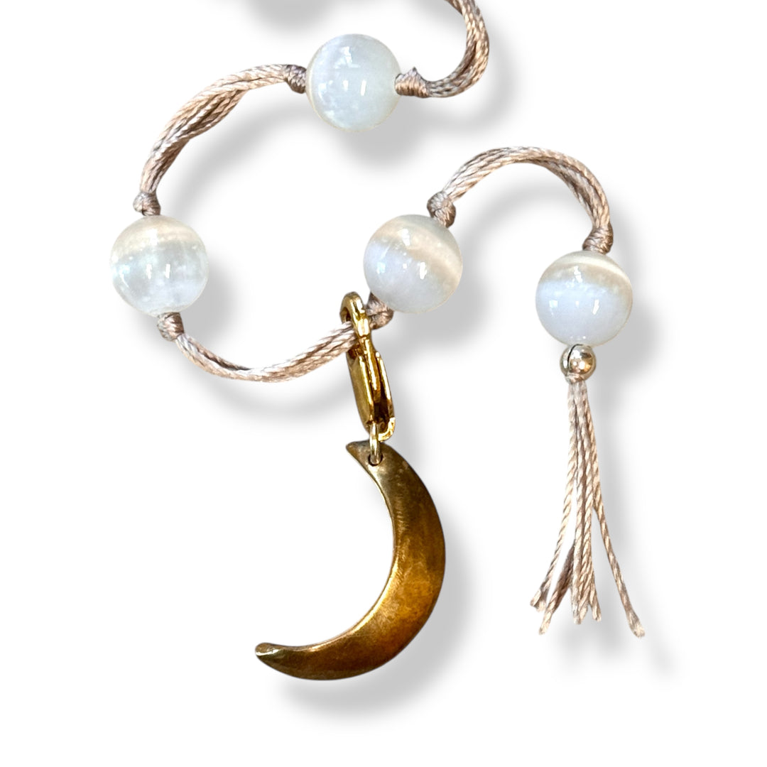 Bracelet with white beads, gold crescent moon charm, and tassel on a white background
