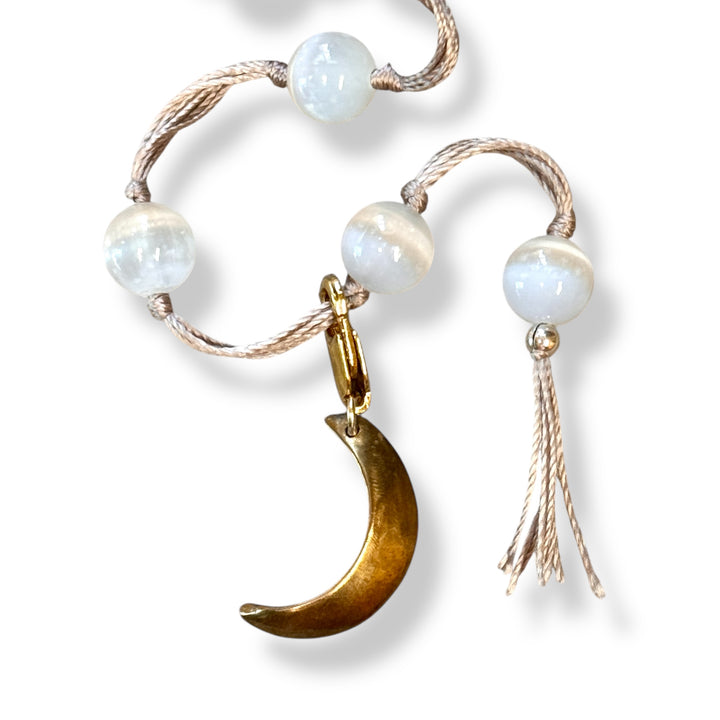 Bracelet with white beads, gold crescent moon charm, and tassel on a white background