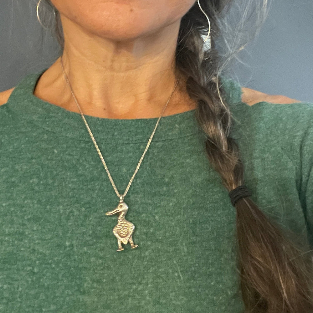 Person wearing a necklace with a bird pendant, against a neutral background