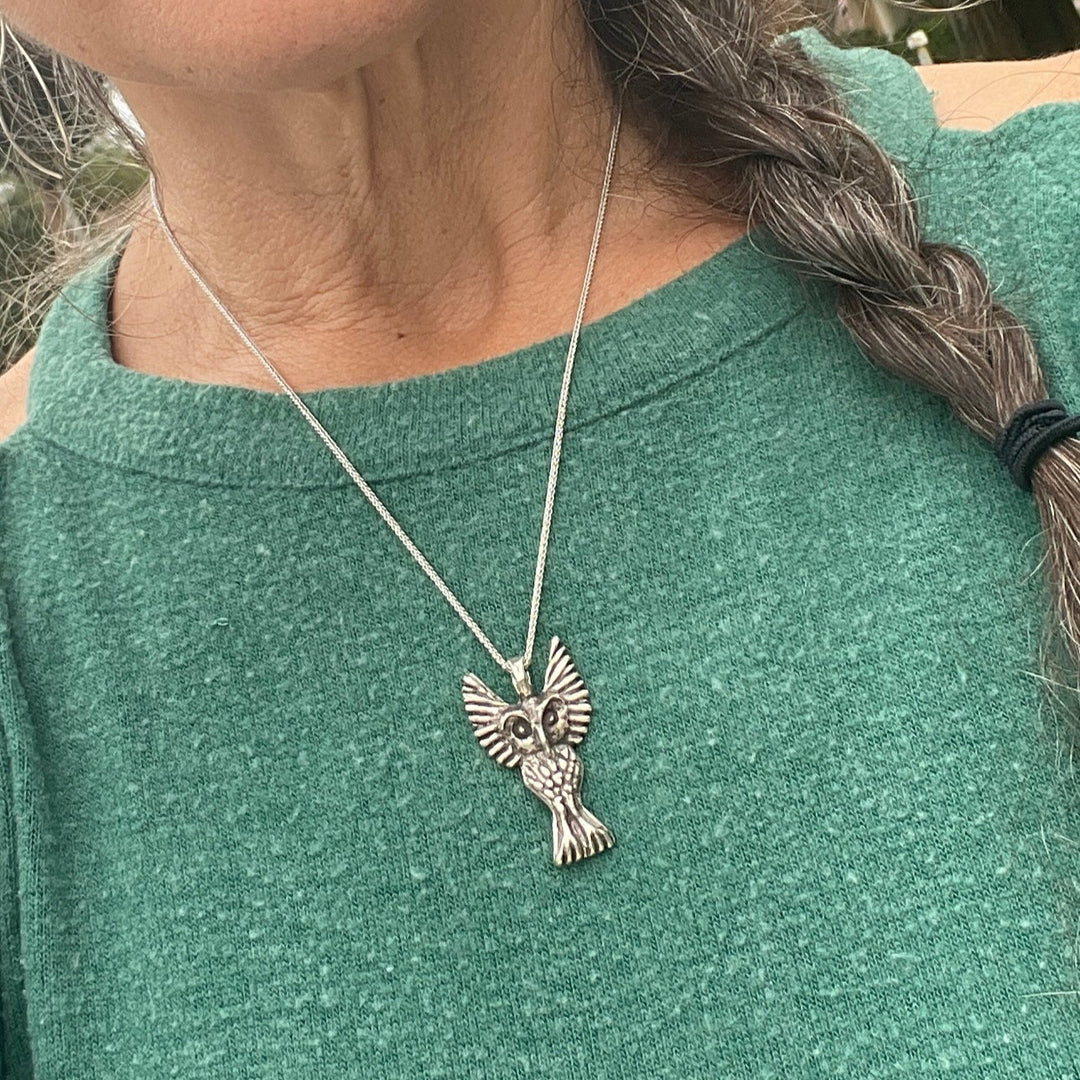Person wearing a green top with a silver necklace featuring an eagle pendant.
