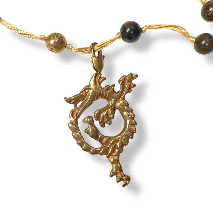 Golden bronze ouroborus pendant on a necklace with brown beads against a white background